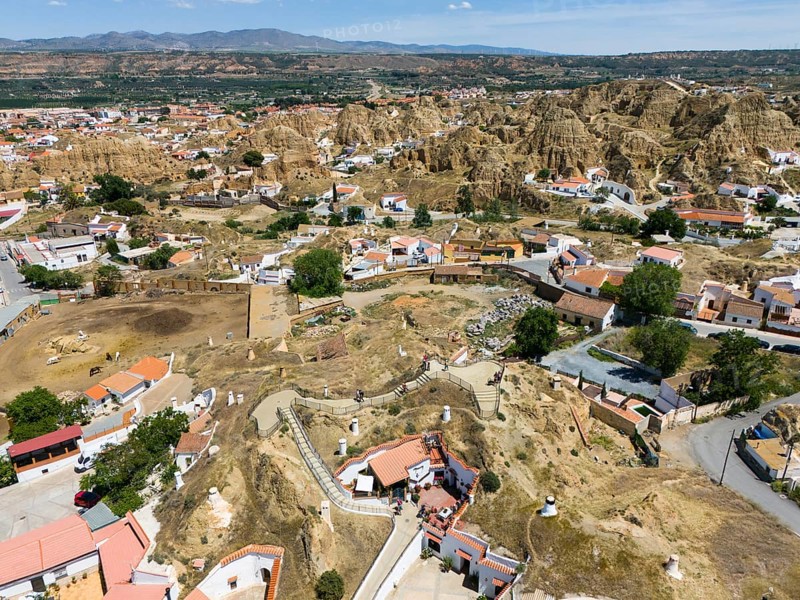 Aerial view of a village surrounded by hilly and stony landscape with mountains in the background, aerial view, cave dwellings, cave neighbourhood, Troglodytos, Guadix, Granada, Andalusia, Spain, Europe