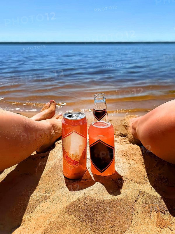 Two people relaxing on a sandy beach with a bottle and can of drink by the water on a sunny day.Belarus, Minsk