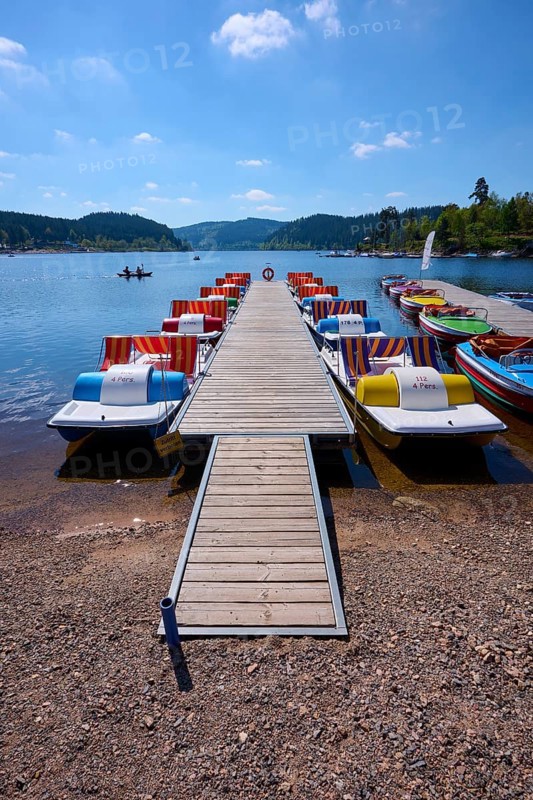 A picturesque scene with colourful pedal boats and wooden boats on a jetty in front of the Schluchsee, surrounded by mountains, spring, Schluchsee, Black Forest, Baden-Württemberg, Germany, Europe