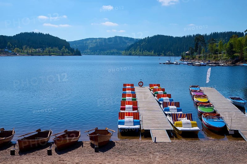 A picturesque scene with colourful pedal boats and wooden boats on a jetty in front of the Schluchsee, surrounded by mountains, spring, Schluchsee, Black Forest, Baden-Württemberg, Germany, Europe