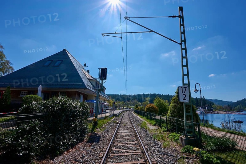 Railway tracks lead through a sunny landscape, surrounded by nature and the Schluchsee, railway station and buildings in the background, spring, Schluchsee, Black Forest, Baden-Württemberg, Germany, Europe