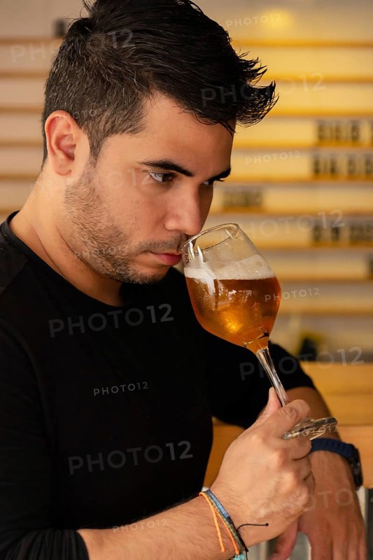 A young Latino man enjoys craft beer in a pub, concentrating on the aroma of the lager he is tasting. His appreciation of the beer's fragrance highlights his passion for good beer and craft beer culture