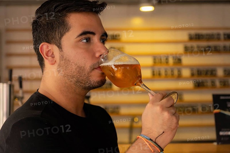 Close-up of a young Latino enjoying a glass of beer in a pub. His satisfied expression and relaxed attitude highlight the social and informal atmosphere of the place, emphasizing the pleasure of savoring a refreshing drink