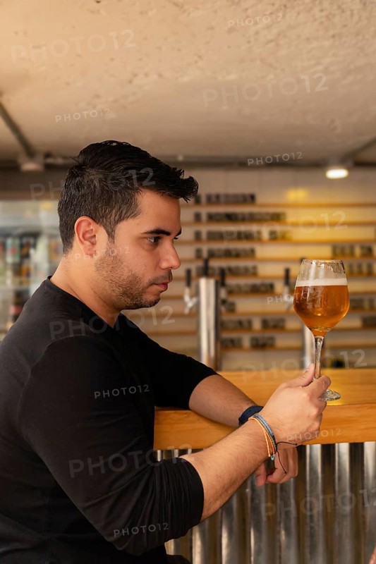 A Latino man in profile, looking appreciatively at his craft lager beer. The image captures his enjoyment and concentration on the quality of the beer, reflecting a moment of sophisticated tasting