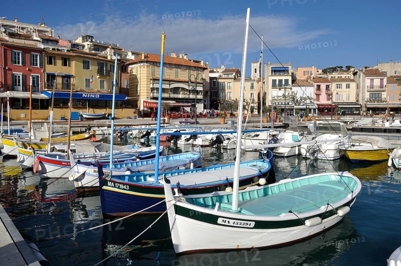 Colorful boats in a vibrant harbor with Mediterranean-style buildings under a clear blue sky, Cassis, the port