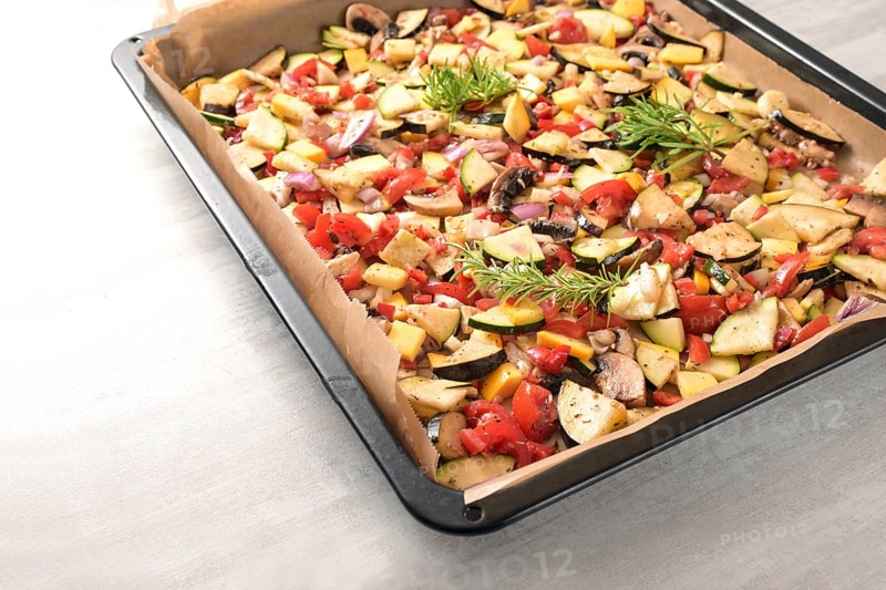 Oven vegetables on a baking tray with zucchini, bell pepper, eggplant, tomato and rosemary garnish, healthy vegetarian meal for low carb diet, copy space, selected focus, narrow depth of field