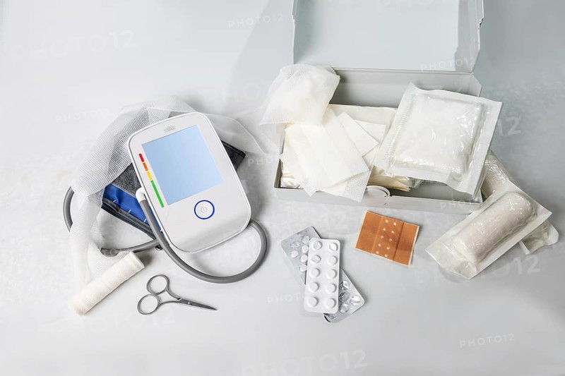 Medical supplies for first aid and the home medicine chest like blood pressure gauge, bandages, plasters, pills and scissors, light gray background, high angle view, copy space, selected focus