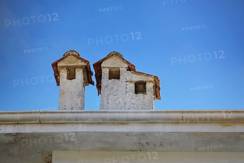 Light plastered chimneys with tiled roofs on a building in Greece, looking like little houses, blue sky with copy space, selected focus