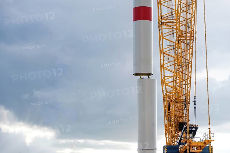 Crane is moving a tower part of a wind turbine onto the first tube guided by people inside, precision work in heavy industry, power plant for renewable energy, cloudy sky, copy space, selected focus