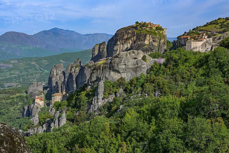 Meteora landscape with four Monasteries situated at the top of various rocky cliffs, famous tourism destination in Greece, valley and high mountains in the background, blue cloudy sky, copy space