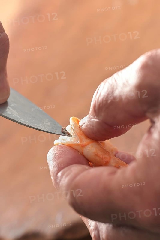Hand holding a shrimp and removes the guts with a knife, preparation for cooking a seafood meal, copy space, closeup, selected focus, very narrow depth of field