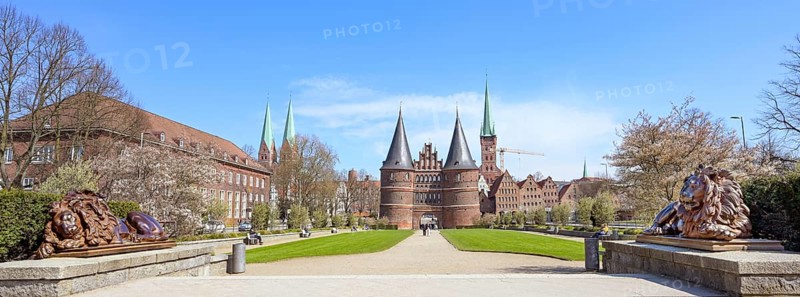 Wide panorama of the Lubeck Holstentor or Holsten gate park with two lion sculptures in front of the famous historic landmark, entrance to the old town of Luebeck, Germany, blue sky, copy space, Europe
