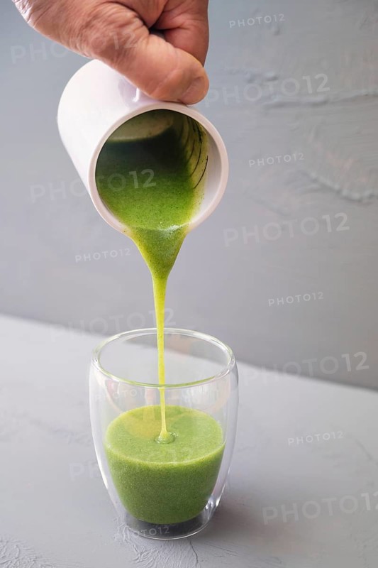 Green smoothie or soup made from wild herbs and vegetables is poured into a double-walled drinking glass against a gray background, healthy food concept, copy space, selected focus