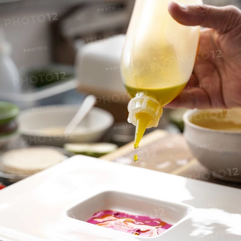 Gourmet chef dripping precious oil from a bottle into a beetroot sauce to prepare a menu course on a white plate, creative cooking concept, selected focus, narrow depth of field