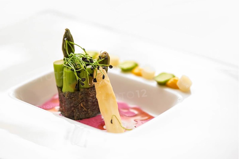 Vegetable course of a gourmet menu made of green asparagus wrapped in a nori seaweed leaf, beetroot dressing and leek sprouts on a white plate, copy space, selected focus, narrow depth of field