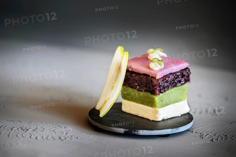 Fish appetizer, layered dish from square-cut pink soused herring, red onion, cucumber, cream gelatin and a slice of apple, modern course in a gourmet menu, gray background, copy space, selected focus
