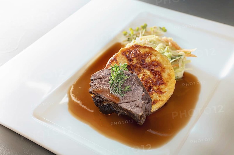 Roast deer, flat bread dumpling and round shaped cabbage vegetable with brown sauce and thyme garnish on a white plate, main course in a menu, copy space, selected focus, narrow depth of field
