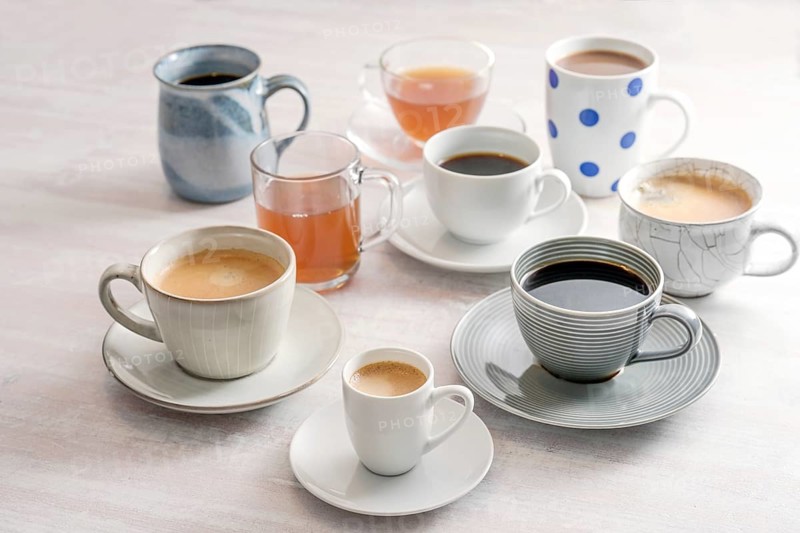 Group of different cups and mugs with coffee and tea drinks on a light table, selected focus, narrow depth of field