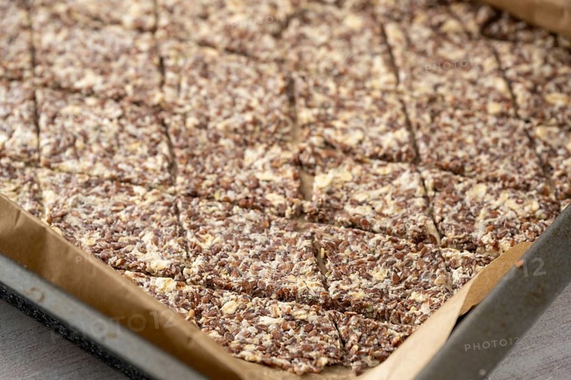 Baking tray with dough from linseed, oat flakes and cheese, cut into rhombs to make healthy crispy pastry snacks, copy space, selected focus, narrow depth of field