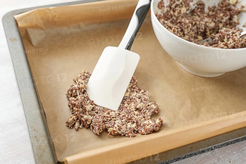 Dough made from flaxseed and oat flakes is spread on a tray with baking paper to make healthy crispy pastry snacks, selected focus, narrow depth of field
