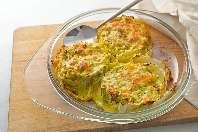 Baked slices of Chinese or napa cabbage in a glass casserole on a wooden kitchen board, creative vegetarian dish, copy space, selected focus, narrow depth of field