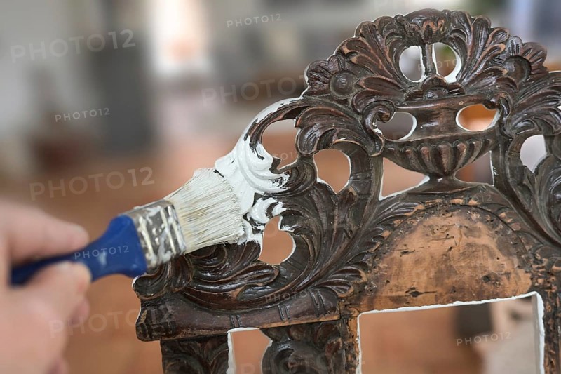 Painting an old chair made of dark decorated wood with a paint brush and white color to get a furniture in shabby chic style, homemade interior design, copy space, selected focus, narrow depth of field