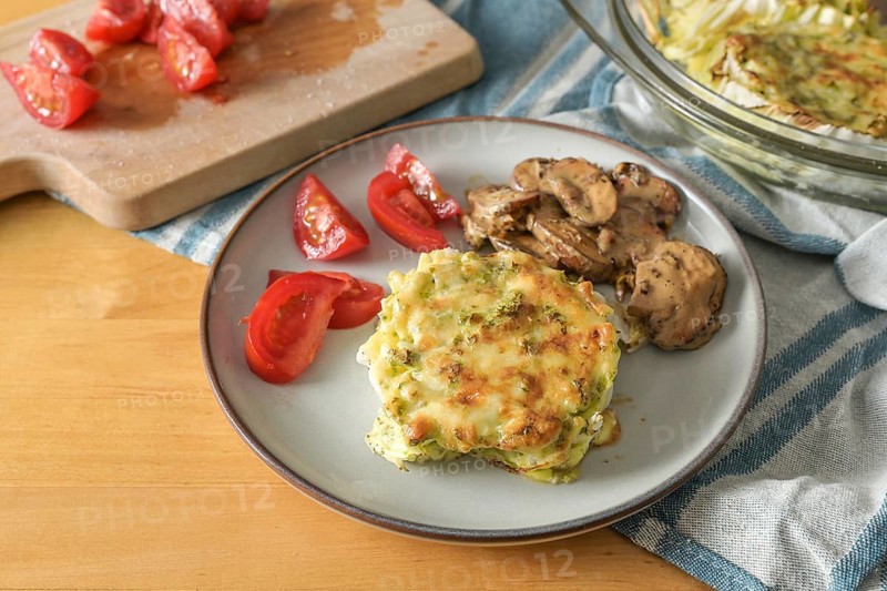 Gratinated Chinese cabbage with mushrooms and tomatoes, healthy vegetarian dish on a wooden table, copy space, selected focus, narrow depth of field