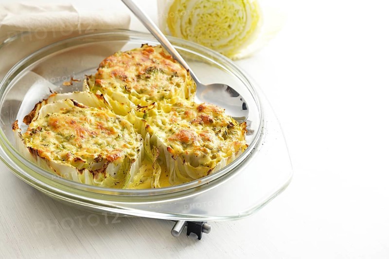 Chinese or napa cabbage gratinated in a glass casserole on a light gray table, healthy cooking, homemade vegetarian meal, copy space, selected focus, narrow depth of field