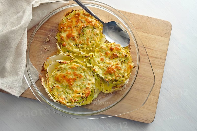 Gratinated slices of Chinese or napa cabbage in a glass casserole on a wooden kitchen board, creative vegetarian dish, high angle view from above, copy space, selected focus