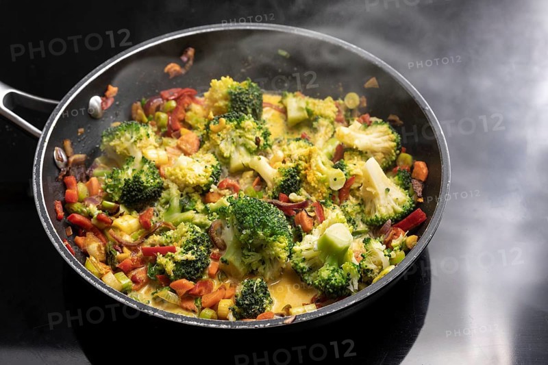 Vegetarian curry with broccoli and other vegetables in a steaming frying pan on a black stovetop, Asian cooking concept, copy space, selected focus, narrow depth of field
