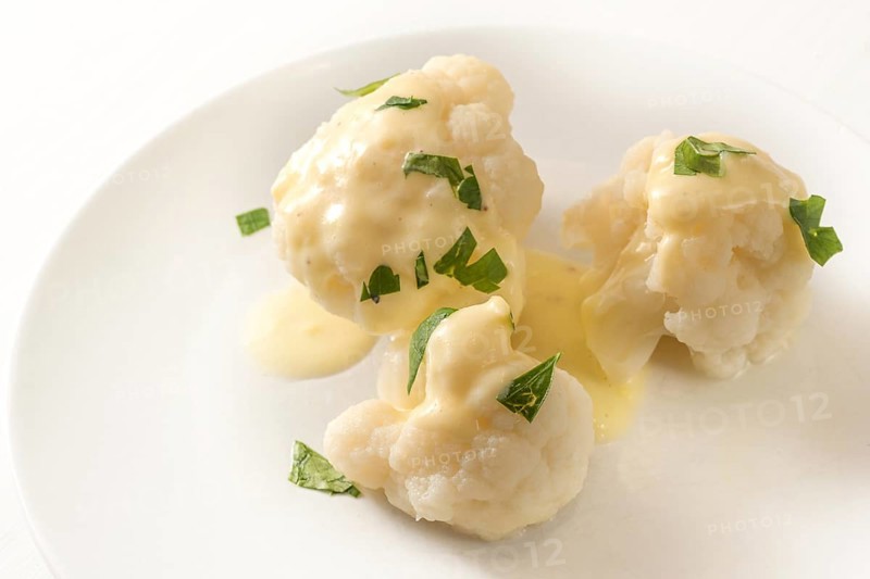 Cooked cauliflower with hollandaise sauce and parsley garnish on a white plate, vegetable side dish, copy space, selected focus, narrow depth of field
