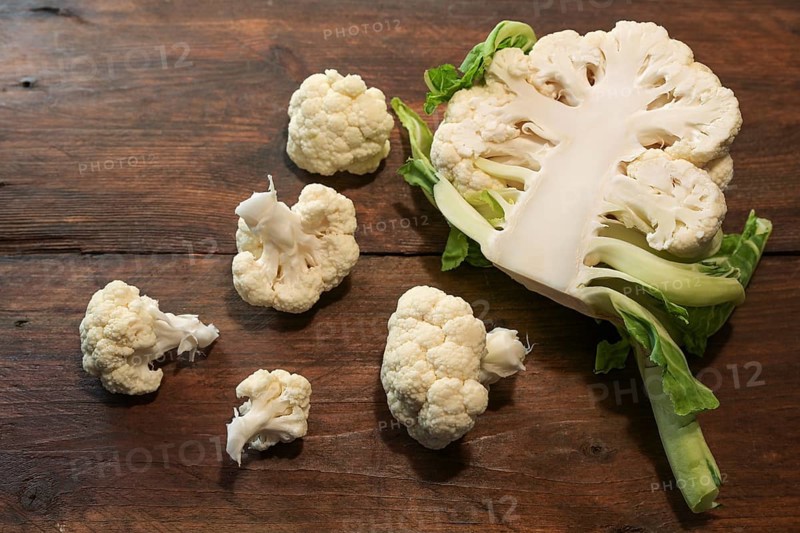 Halved raw cauliflower and some pieces on a dark rustic wooden table, healthy food concept, copy space, view from above, selected focus, narrow depth of field