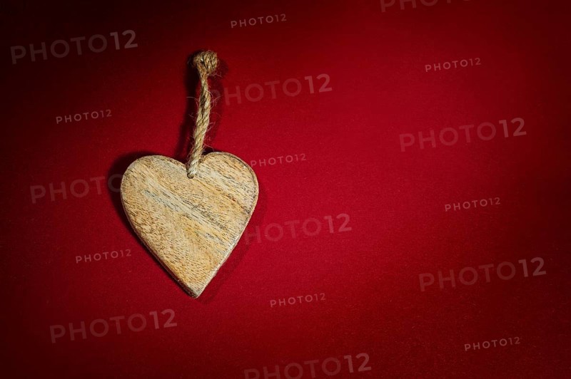 Simple heart shape made of wood with a rustic cord on a background of dark red felt, holiday greeting card and love symbol for valentines day, fathers or mothers day, copy space, selected focus