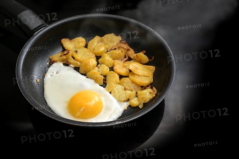 Fried egg and roast potatoes in a black frying pan on the stove in the kitchen, simple cooking, copy space, selected focus, narrow depth of field