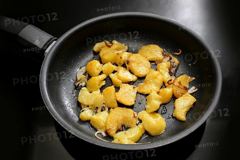 Potato slices and onion are roasted in a black frying pan on the stove, in Germany called Bratkartoffeln, food and cooking theme, selected focus, narrow depth of field
