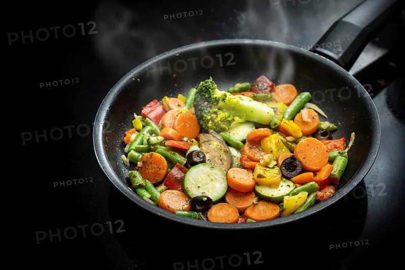 Stir fry vegetables in a black pan with carrots, zucchini, broccoli, green beans, olives and herbs, healthy vegetarian meal Mediterranean style, copy space, selected focus, narrow depth of field