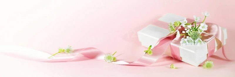 Romantic love gift with ribbon and white flowers on a pink peach background in panoramic format for Valentines day, Mothers day, birthday or Wedding, copy space, selected focus, narrow depth of field