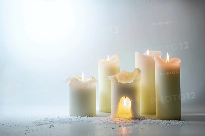 Group of white candles, one is burning overhead in a warm cave, surreal still life as energy saving concept, don't waste the heat outside, light gray background, copy space, selected focus