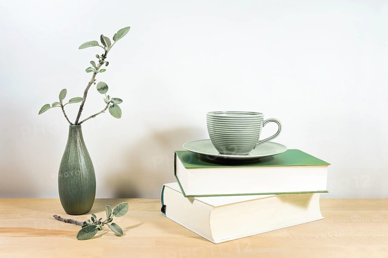 Wooden desk or table with books, a green tea cup and sage twigs in a small ceramic vase against a gray white wall, copy space, selected focus, narrow depth of field