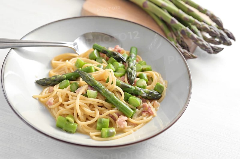 Spaghetti with green asparagus, bacon and egg as carbonara sauce variation on a gray plate and on a white painted wooden table, selected focus, narrow depth of field