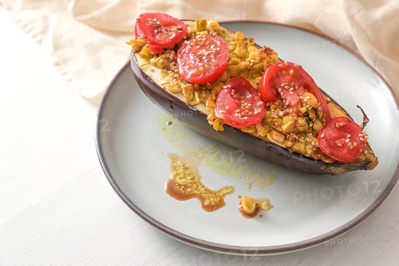 Healthy vegetarian low carb meal, baked eggplant with turmeric, ginger, onions, tomatoes and sesame seed on a plate on a white wooden table, copy space, selected focus, narrow depth of field