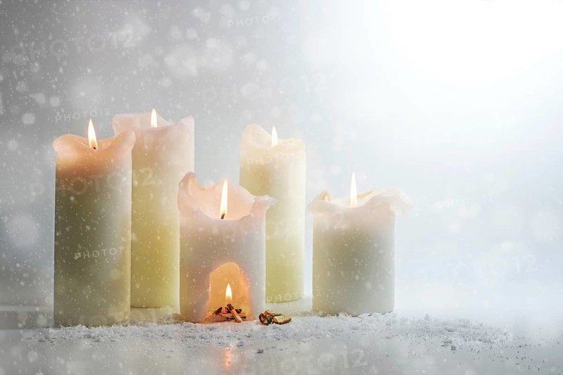 White candles burning in the snow, in one is a carve with a warm campfire, surreal winter still life, heat and energy concept, light gray background, copy space, selected focus, narrow depth of field