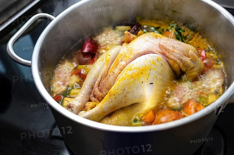 Chicken soup with vegetables and spices is boiling in a pot, cooking a healthy broth, home remedy against cold and flu, selected focus, narrow depth of field