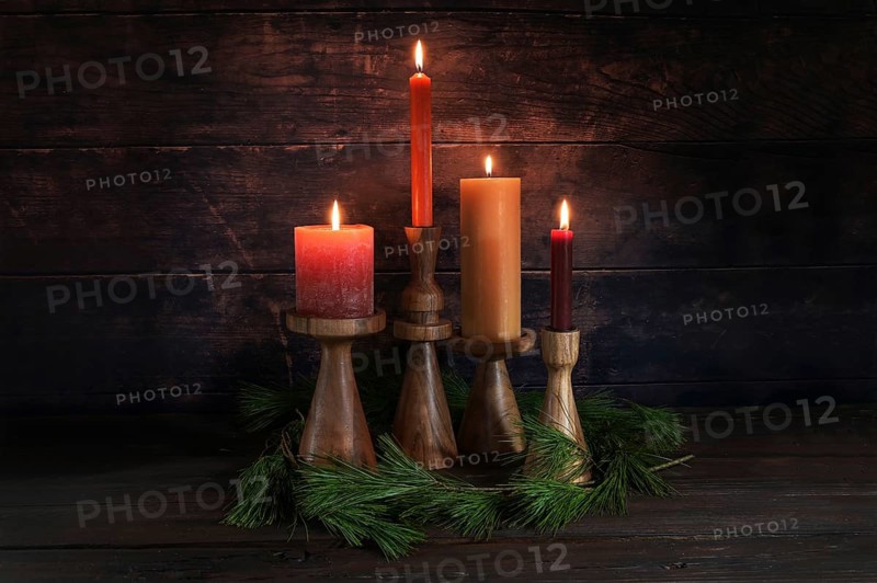 Four different candles in warm colors on wooden stands for Advent with some pine branches against a dark rustic background of wood, copy space, selected focus