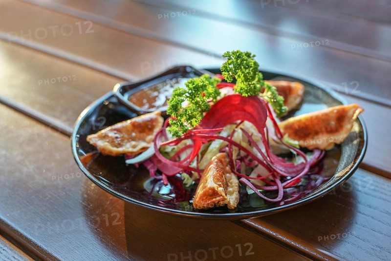 Deep fried gyoza with salad and sauce served as appetizer on a black plate, Asian dish on a wooden table, copy space, selected focus, very narrow depth of field