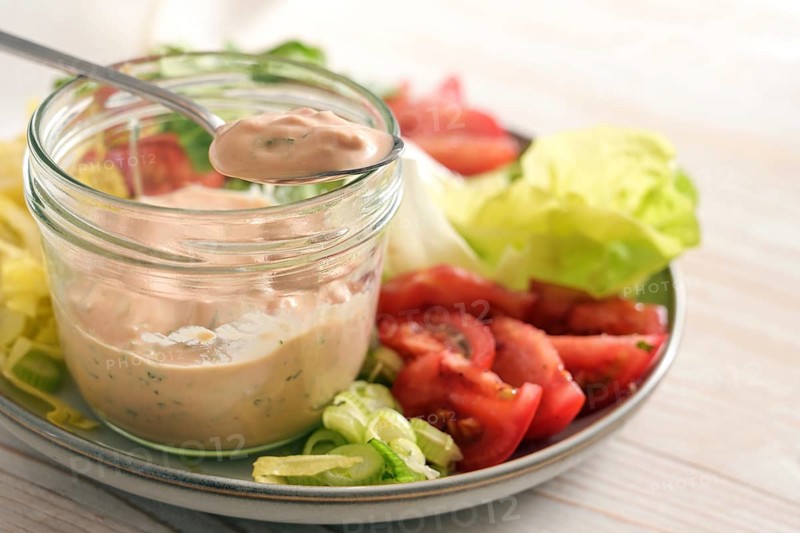 Salad dressing from skyr on a spoon and in a glass jar on a plate with slices of lettuce and tomatoes, healthy raw food meal, selected focus, narrow depth of field