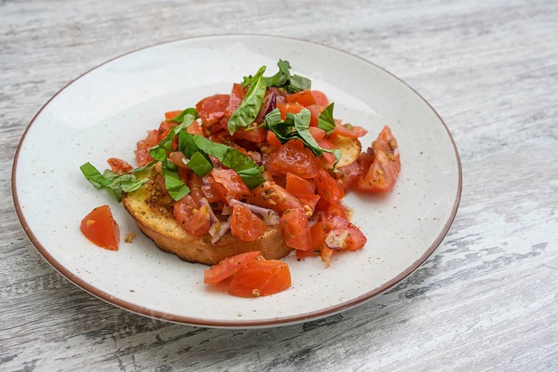 Bruschetta, toasted bread with garlic and olive oil, served with diced tomatoes, onion and basil, popular Italian appetizer on a plate and a grey table, selected focus, narrow depth of field