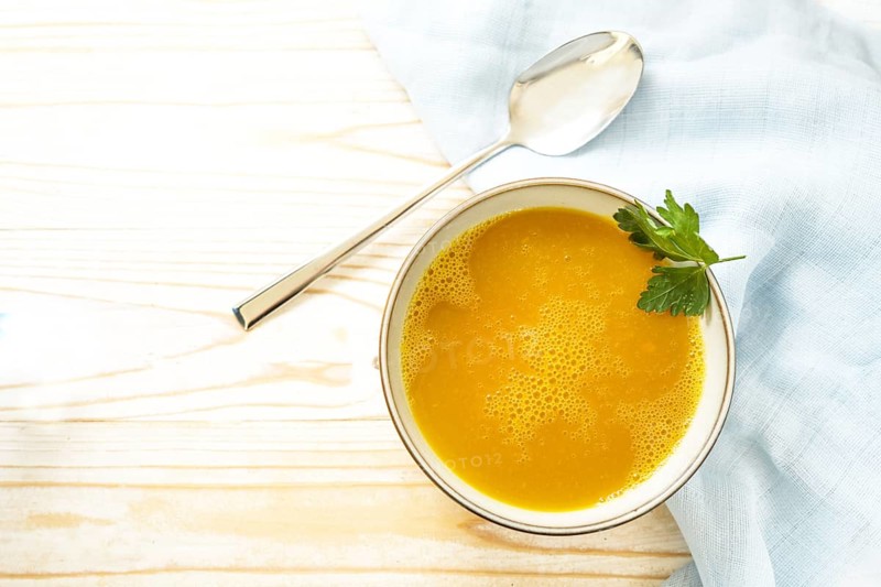 Carrot soup in a bowl on a light wooden table, healthy vegetable meal, recipe by professor Ernst Moro against diarrhea, copy space, high angle view from above, selected focus