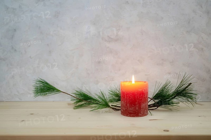 Red candle lit for the first Advent, pine branch as a simple, minimal decoration on a light wooden board against a rustic plaster wall, large copy space, selected focus