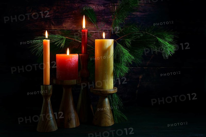 Advent arrangement with four candles in red and yellow on wooden holders and pine branches against a very dark background from rustic wood, copy space